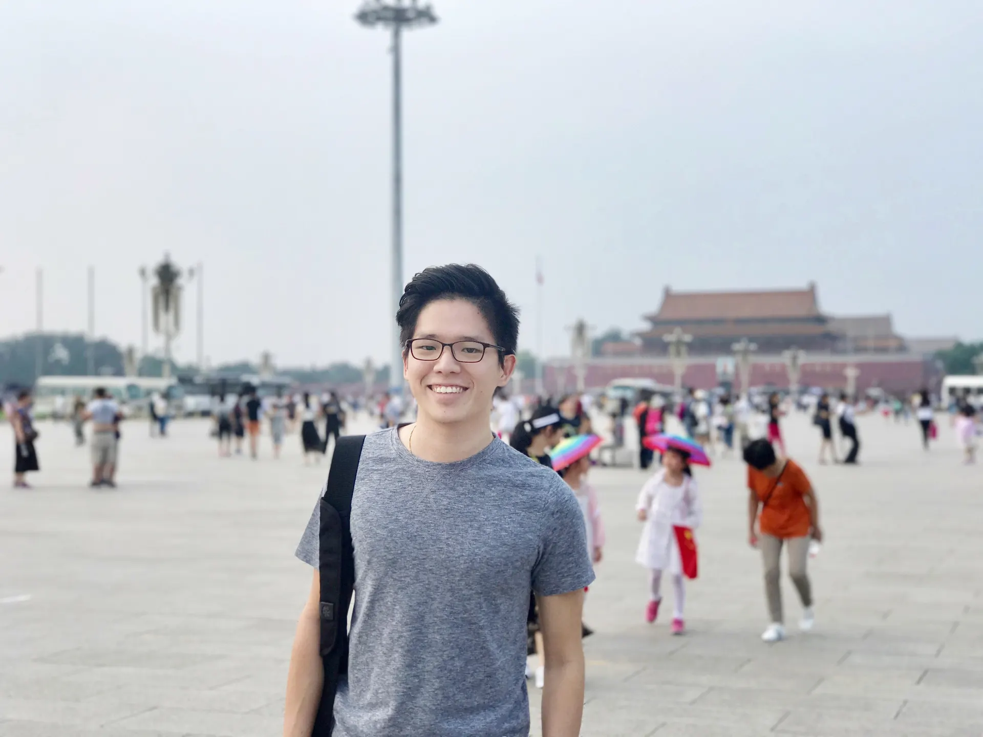 Dr. Jovian Tan smiling in Tiananmen Square, Beijing, with a traditional gate building in the background