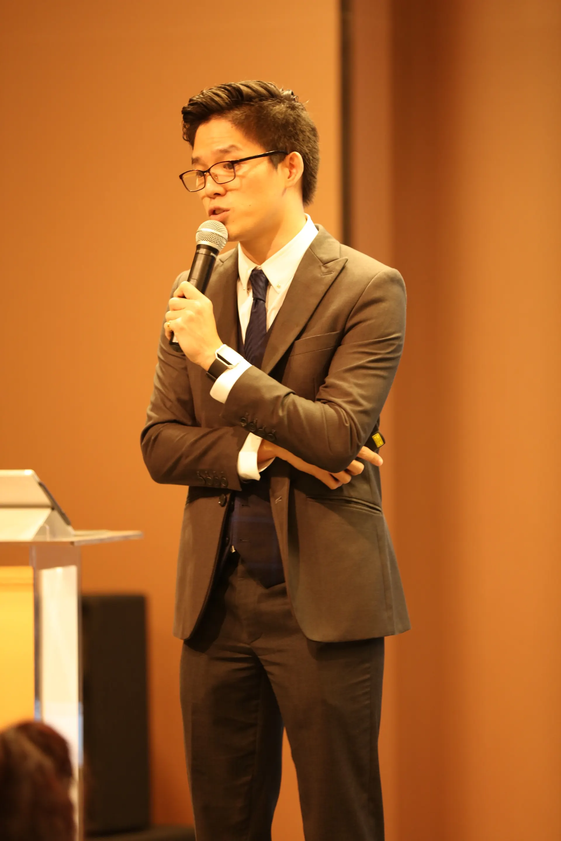 Dr. Jovian Tan in a grey suit speaking into a microphone beside a lectern