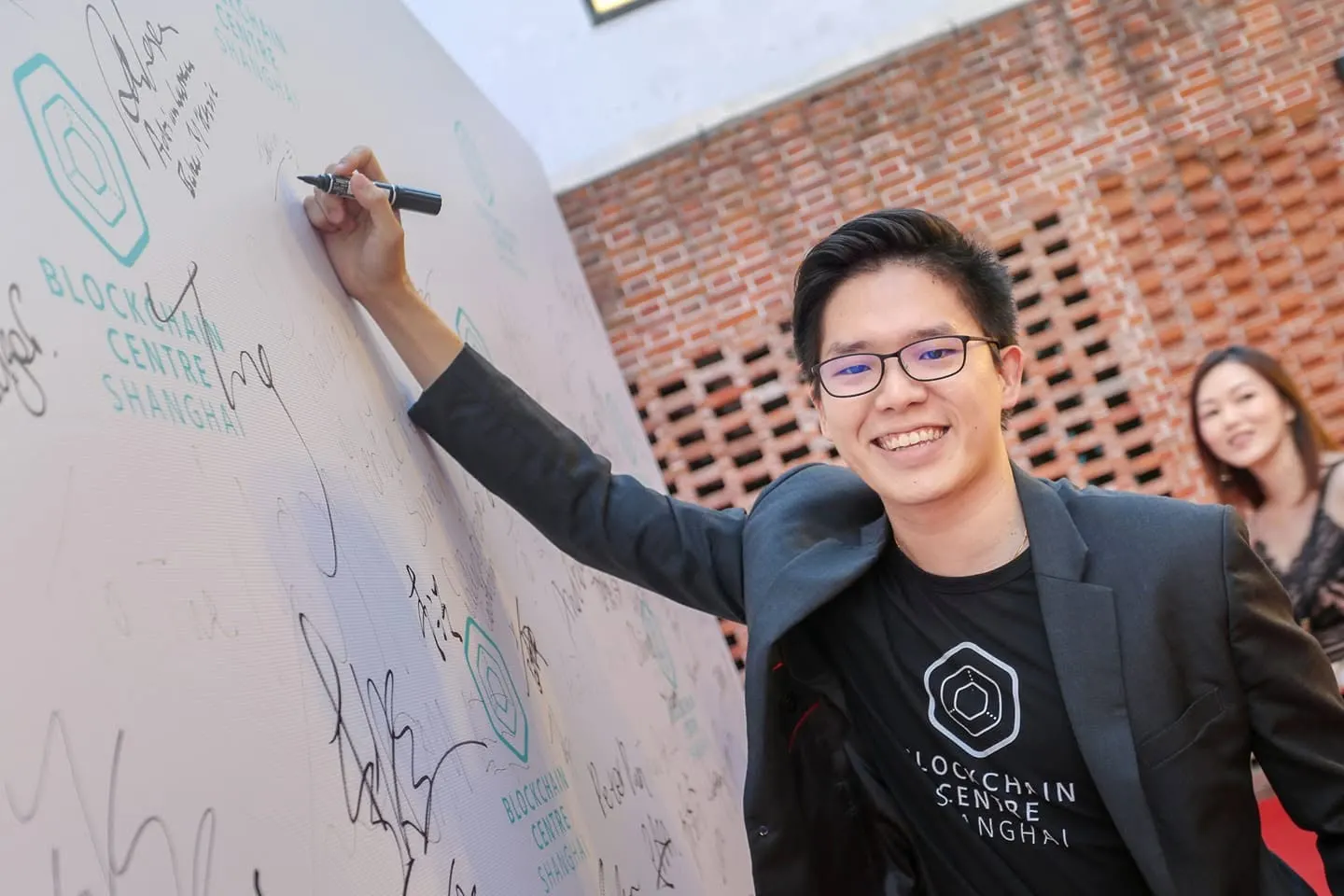 Dr. Jovian Tan smiling as he signs a guest wall branded Blockchain Centre Shanghai