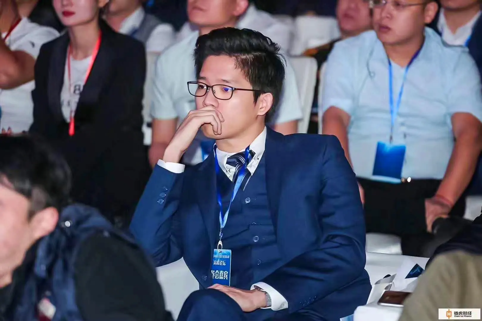 Dr. Jovian Tan in a navy three-piece suit wearing a guest badge, seated and listening in a conference audience