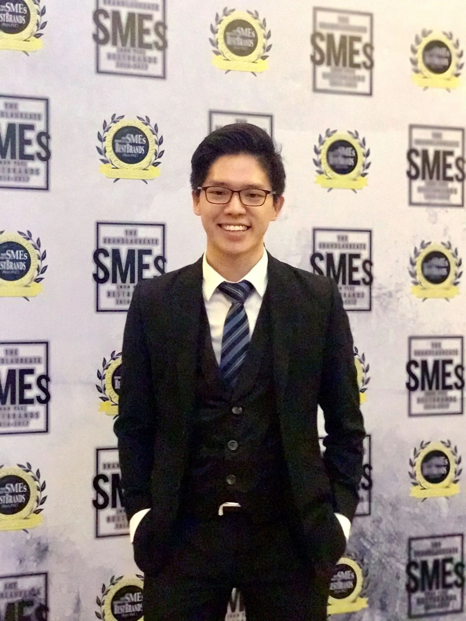 Dr. Jovian Tan in a three-piece suit in front of a BrandLaureate SMEs BestBrands backdrop