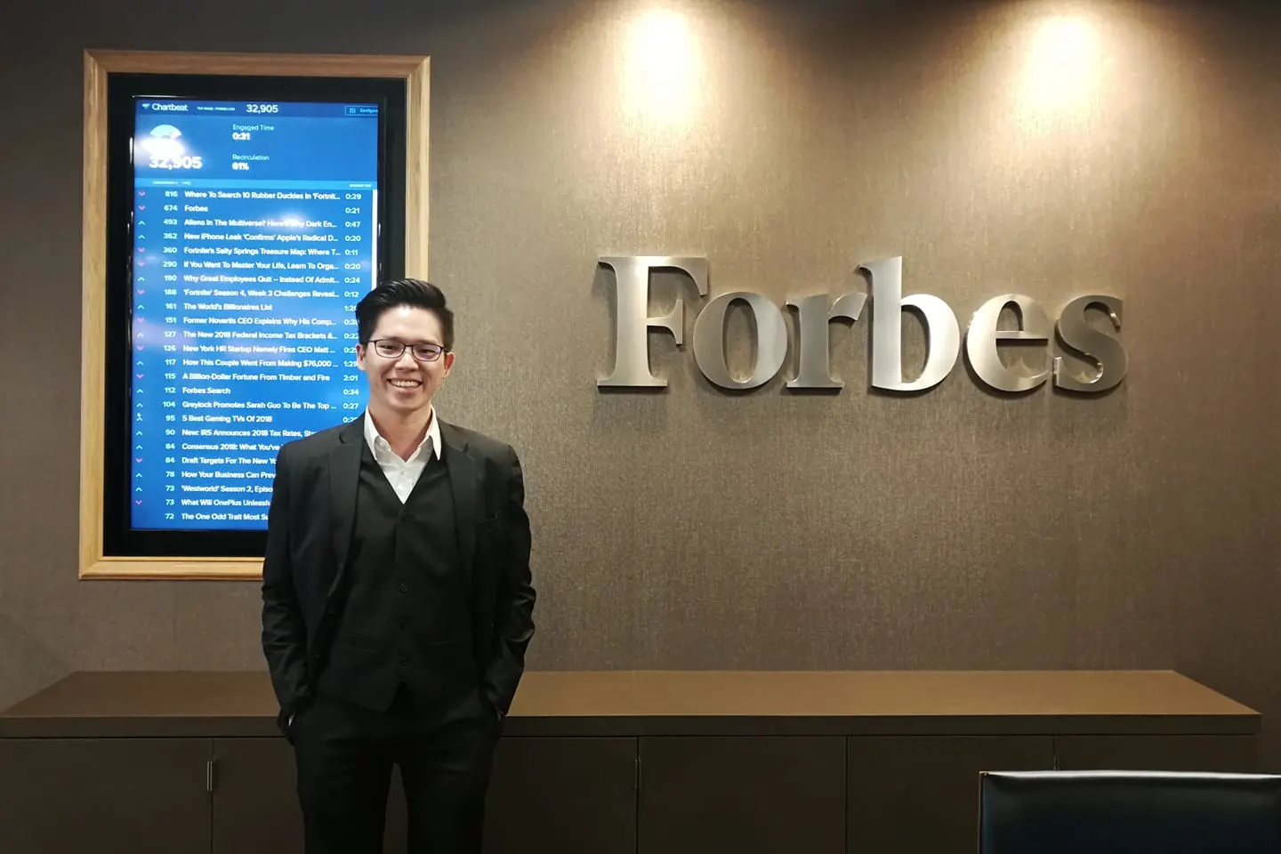 Dr. Jovian Tan standing beside the Forbes logo on an office wall
