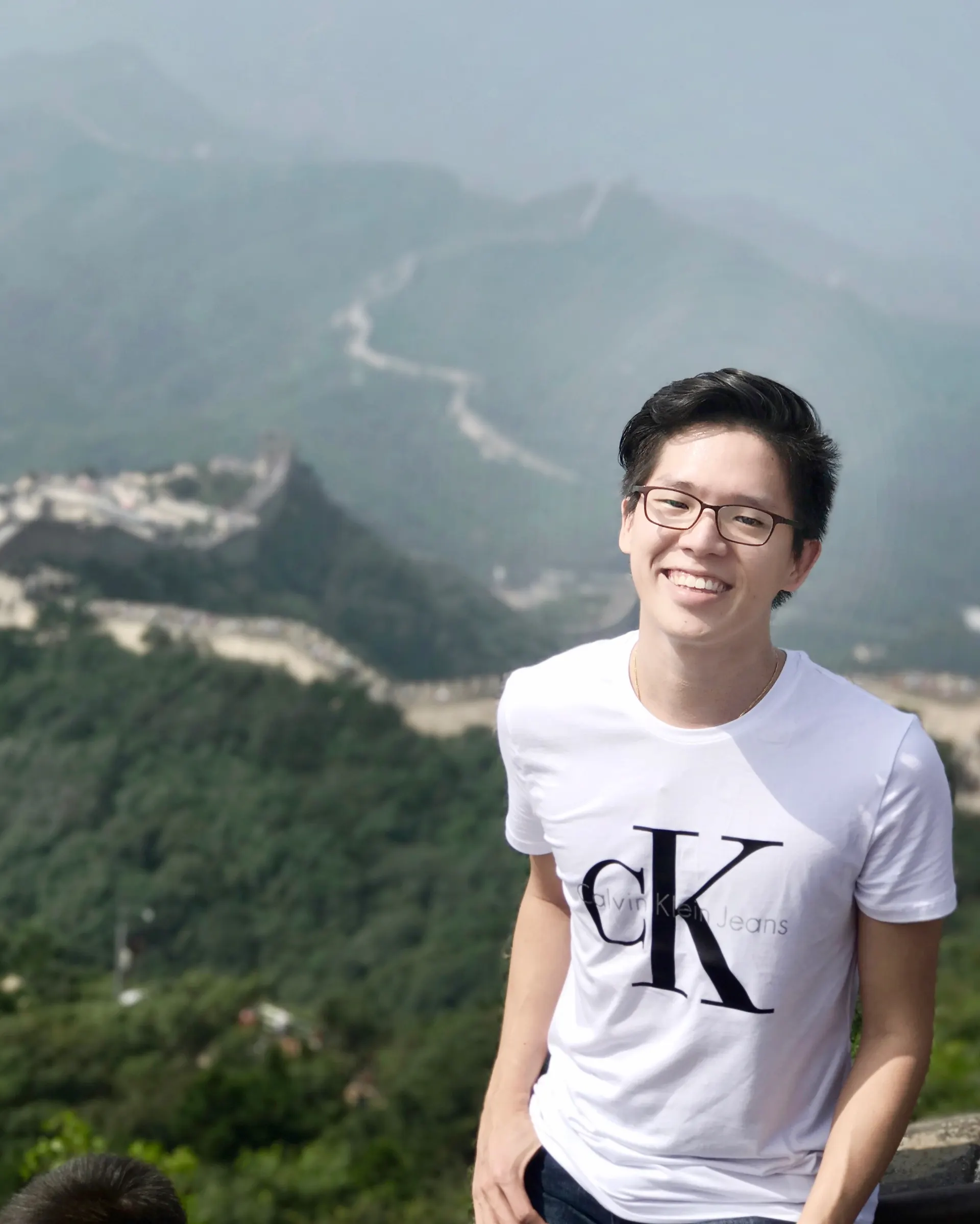 Dr. Jovian Tan smiling in front of the Great Wall of China winding across green hills